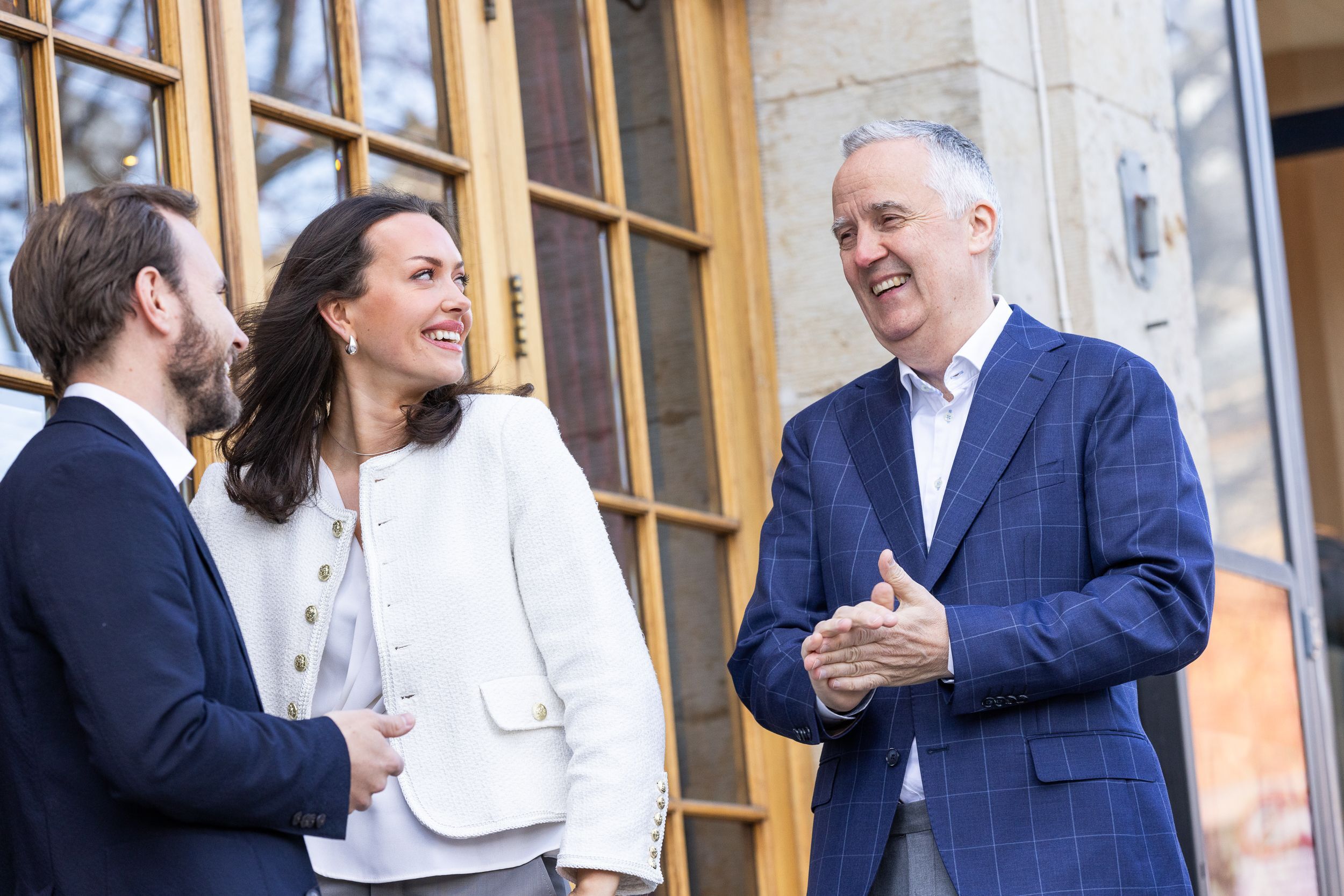 Tre personer står ute og smiler og ler til hverandre